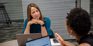 a sitting female with a laptop listing to a female in conversation