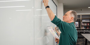 a man wearing a green shirt is writing on a white board