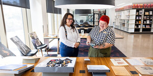 Two people standing in a room filled with sunlight in front of tables displaying archival materials