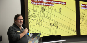A person standing at a podium holding a microphone and talking 